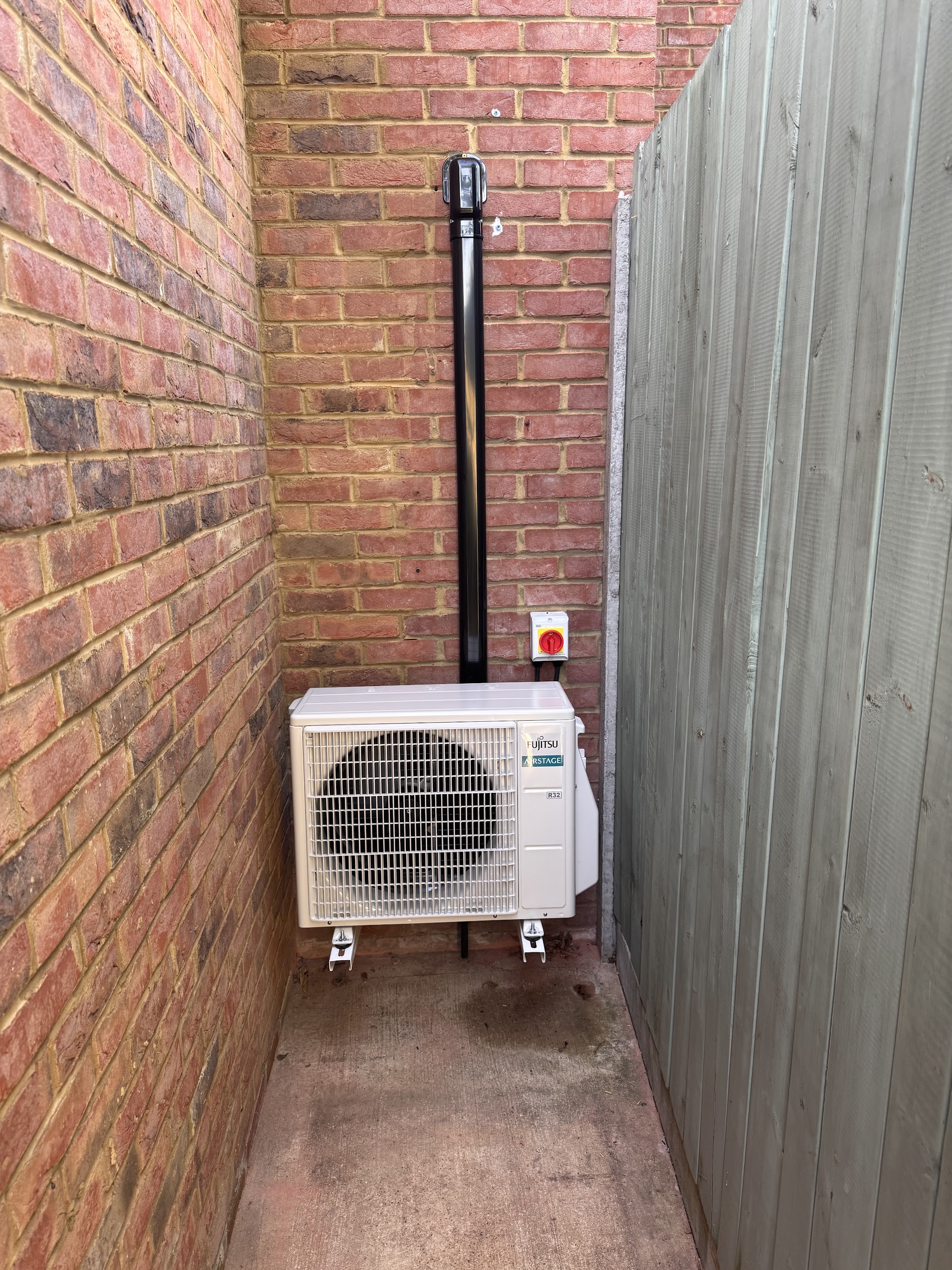 Air conditioning outdoor unit installed in a side passage beside a brick wall