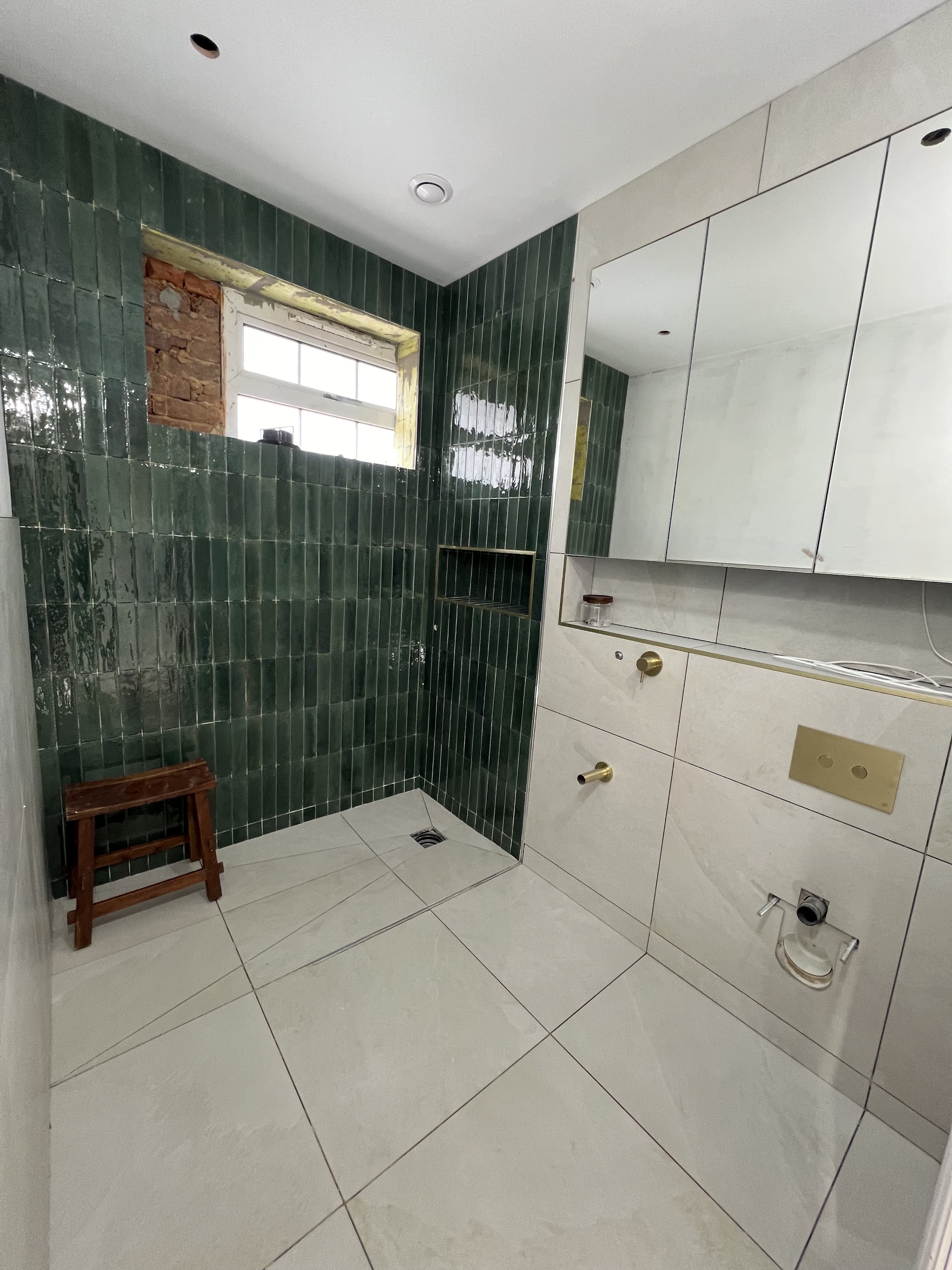 Bathroom being fitted with green wall tiles and a large white floor tile