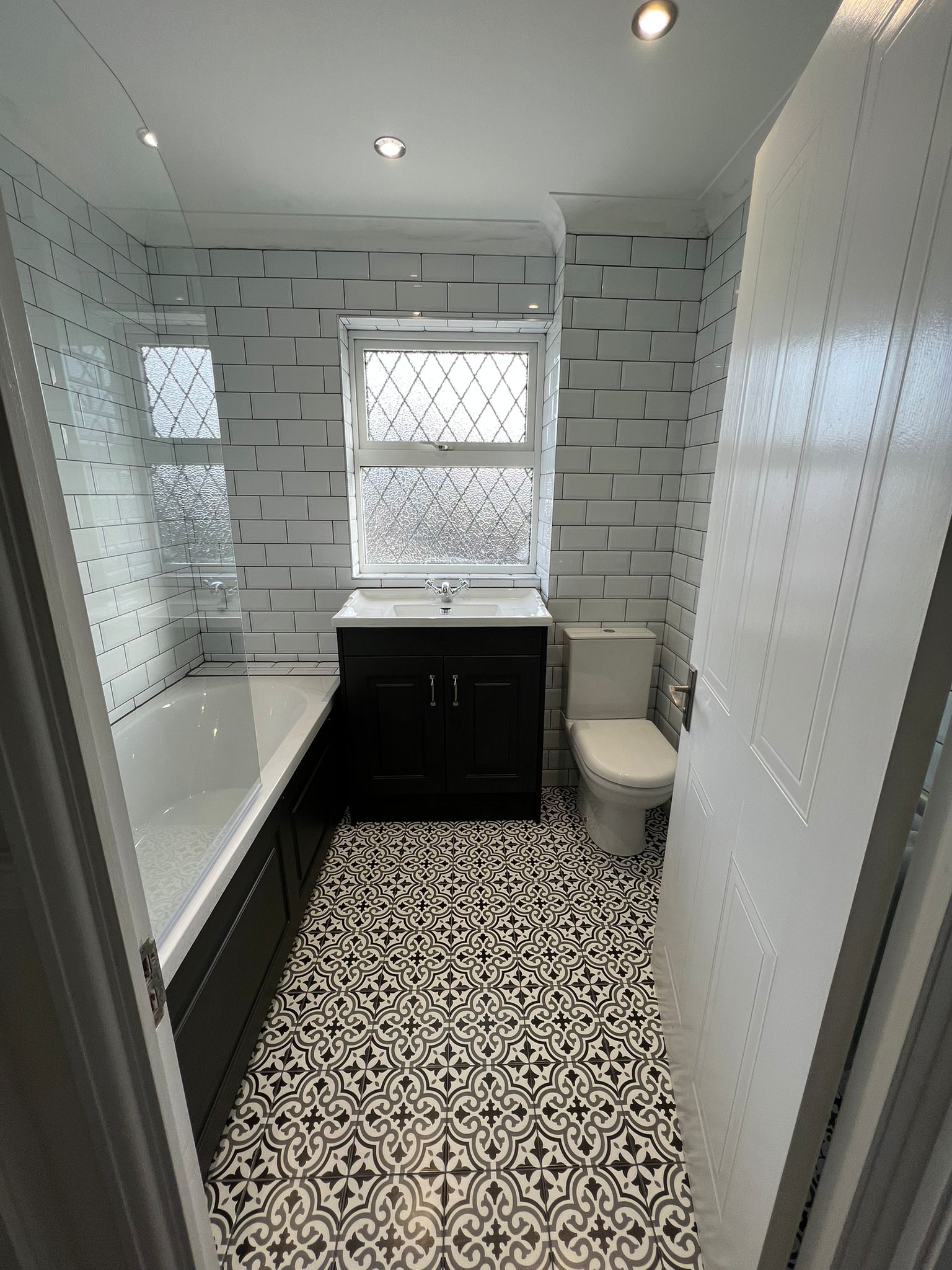 Bathroom with patterned floor tiles, white metro walls and a dark vanity unit