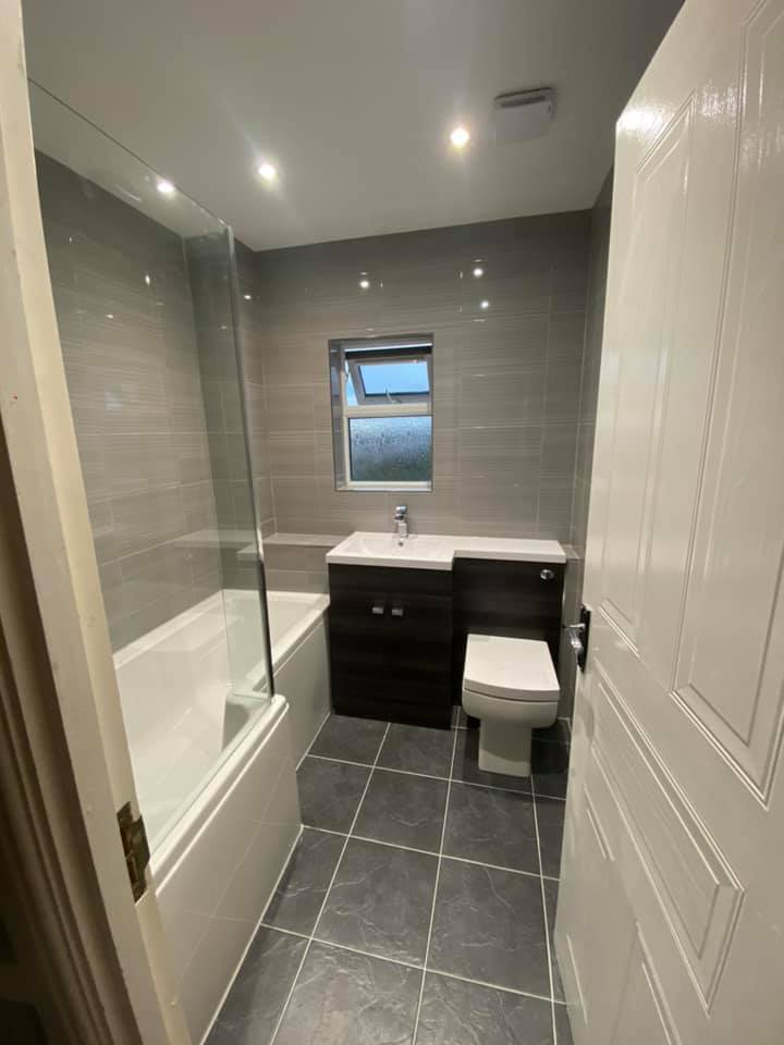 Bathroom with a bath, grey floor tiles and dark vanity unit